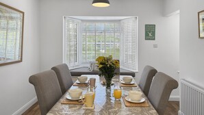 A dining room with a table set for two, white blinds, a hanging light fixture, and a framed inspirational quote on the wall.