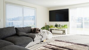A modern living room with a grey sofa, a large flat-screen TV mounted on the wall, and a white console table with plants.