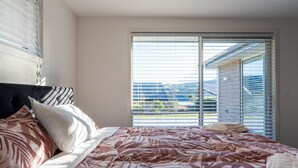 A bedroom with a large bed, a headboard, and a view through the window.