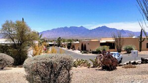 A desert landscape with a row of buildings, a parking area, and mountains in the background. - Enjoy Gorgeous Mountain Views w/Privacy & Southwestern Ambiance Inside and Out! (Green Valley)