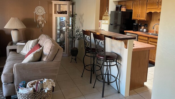 A living room with a sofa, a dining area with a bar, and a kitchen with wooden cabinets and a refrigerator. - Enjoy Gorgeous Mountain Views w/Privacy & Southwestern Ambiance Inside and Out! (Green Valley)