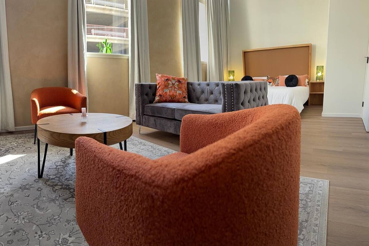Hotellihuone, jossa on sohva, kaksi nojatuolia, pyöreä pöytä ja sänky.