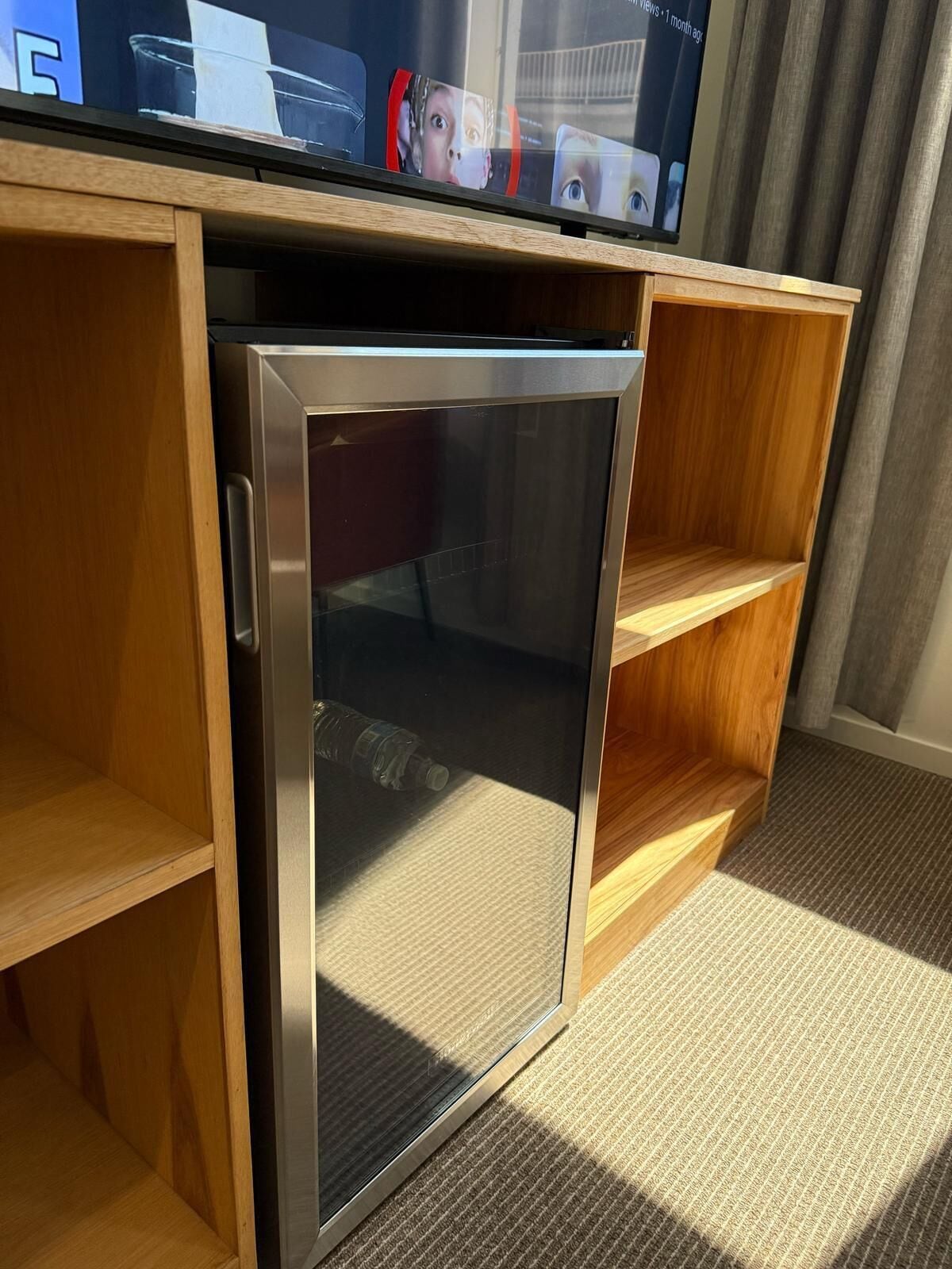 Een compacte koelkast in een hotelkamer met houten planken en een vloerbedekking.