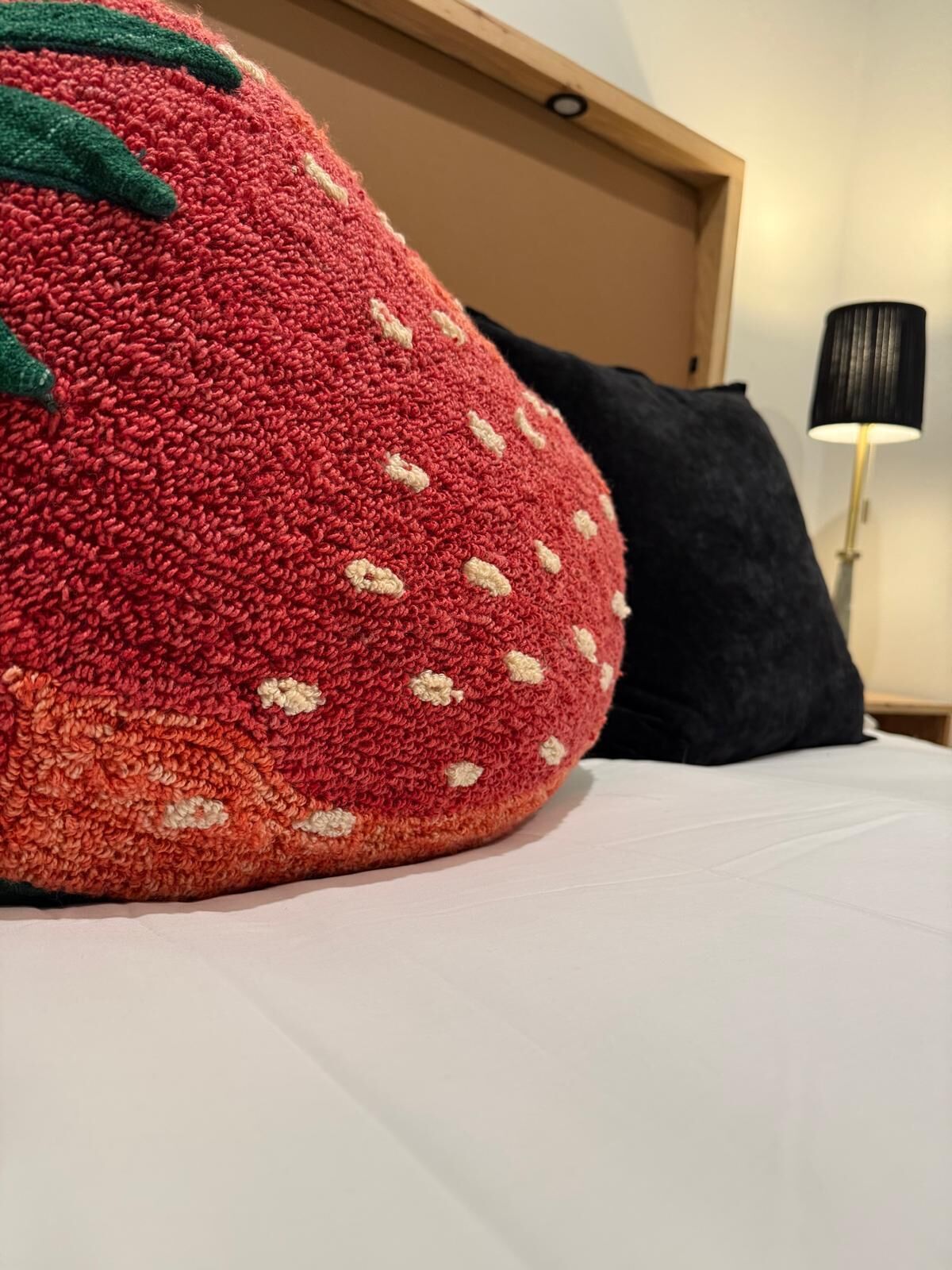 Un almohadón grande con forma de fresa, de textura marcada, sobre una cama con sábana blanca.
