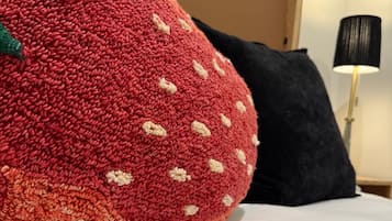 Un almohadón grande con forma de fresa, de textura marcada, sobre una cama con sábana blanca.