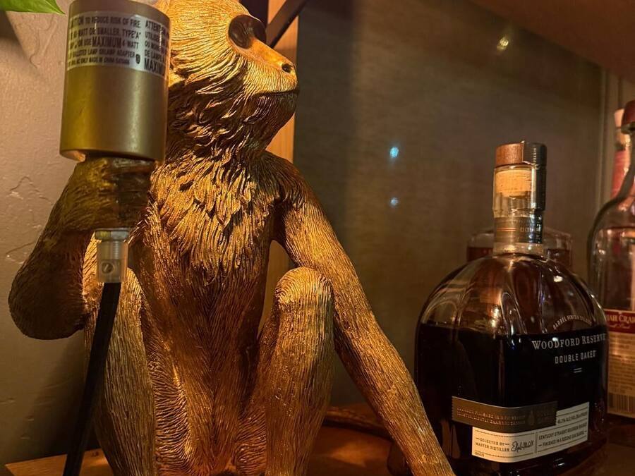 Une sculpture en bois représentant un gorille tenant une ampoule, avec une bouteille de Woodford Reserve Double Oak en arrière-plan.
