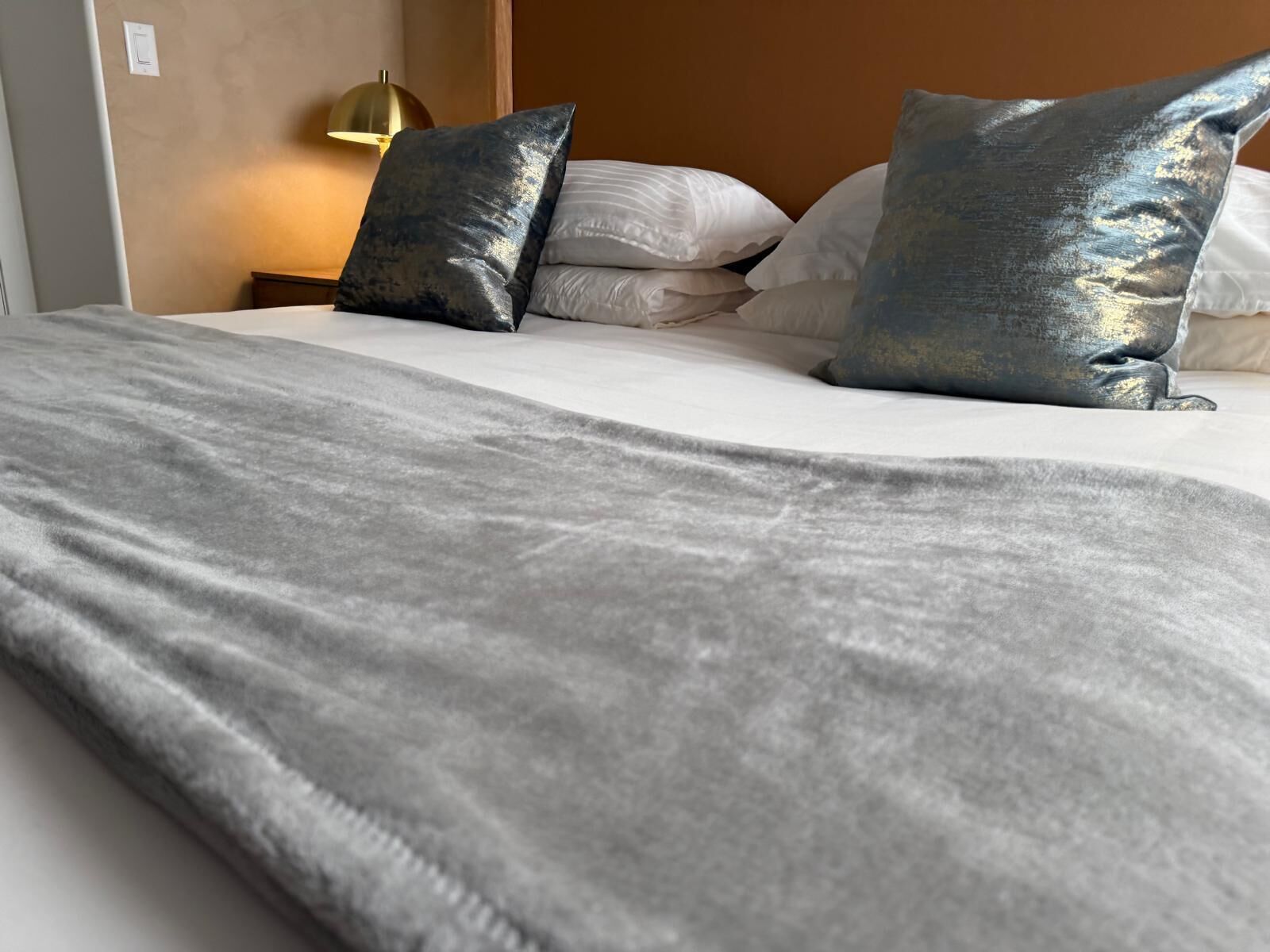 Een net opgemaakt bed met een grijze deken en twee metallic kussens.