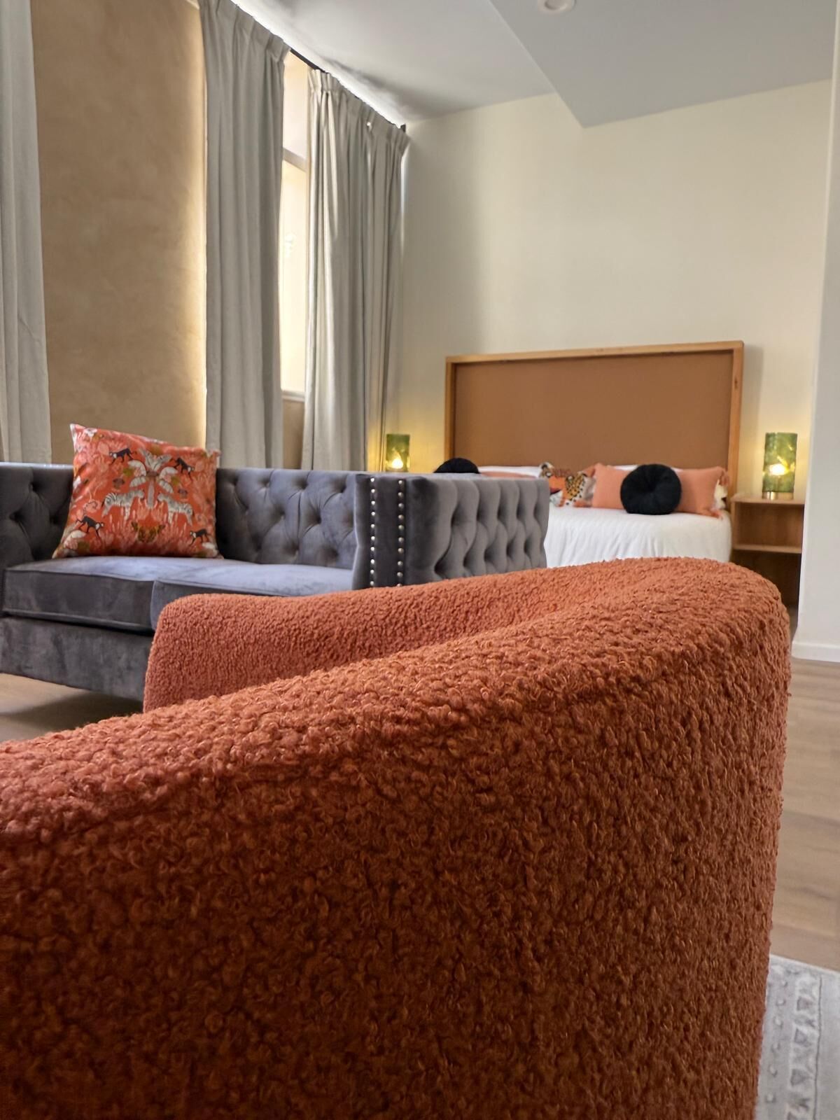 A bedroom with a bed, a grey sofa, and a large orange ottoman.