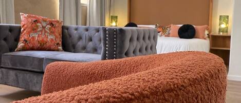 A bedroom with a bed, a grey sofa, and a large orange ottoman.