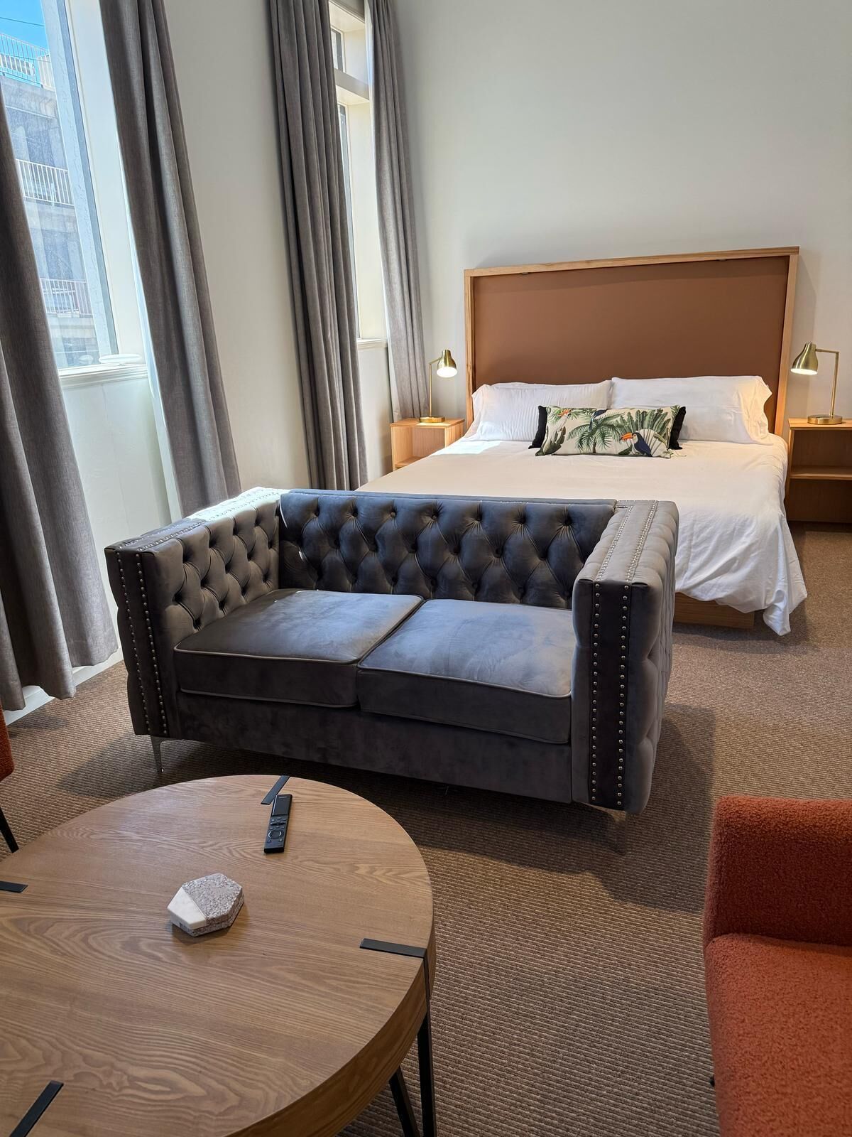 Une chambre d’hôtel avec un grand lit, un canapé capitonné, une table ronde en bois et une petite chaise orange.