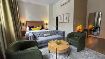 A hotel room with a bed, a sofa, two armchairs, a coffee table, and a dining area with a table and chairs.