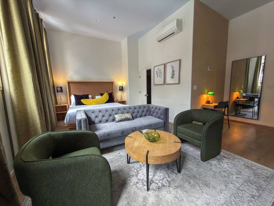 A hotel room with a bed, a sofa, two armchairs, a coffee table, and a dining area with a table and chairs.