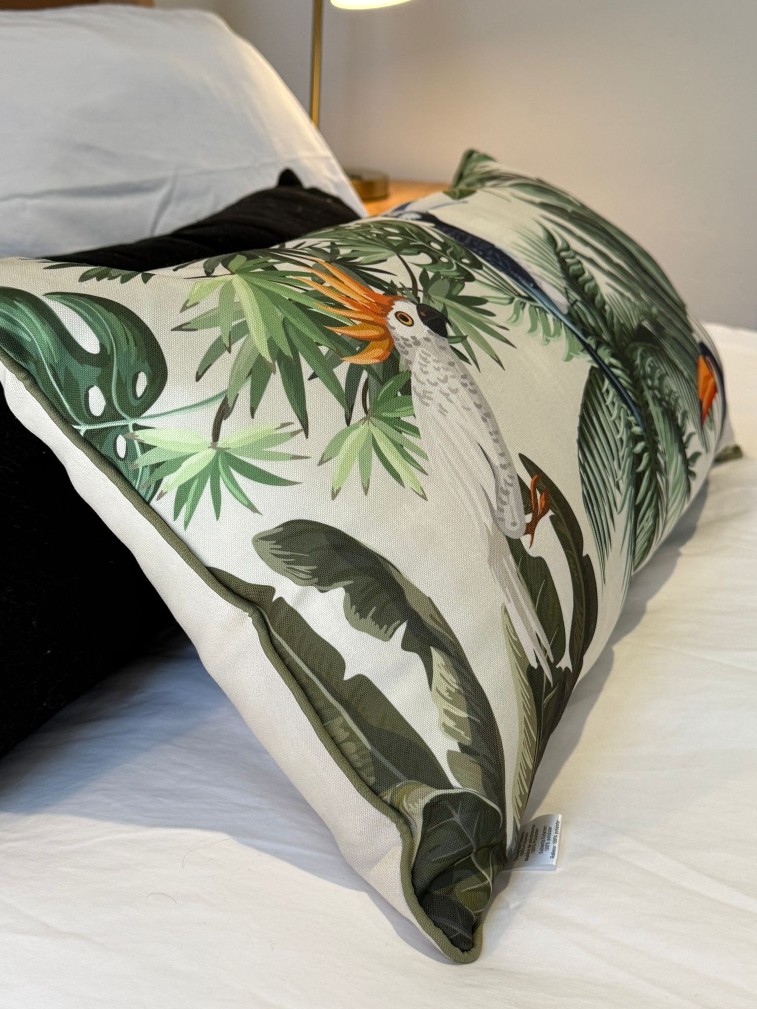 A pillow with a tropical bird and leaf pattern on a bed.