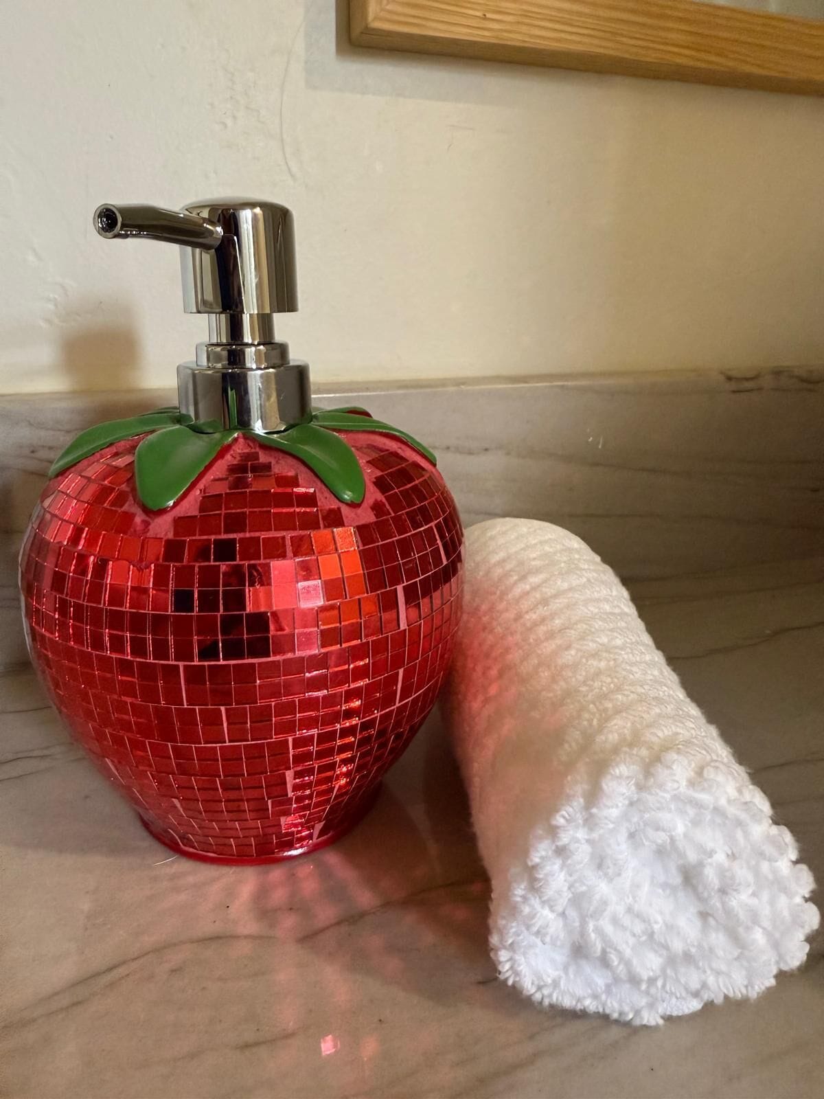 Eine rote Discokugel mit einer Pumpflasche und einem weißen, flauschigen Gegenstand auf einer Marmorplatte.