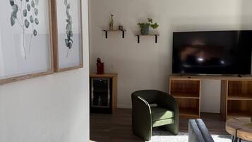 Un salon moderne avec un téléviseur à écran plat, un fauteuil vert, un canapé gris et des étagères en bois ornées d’objets décoratifs.