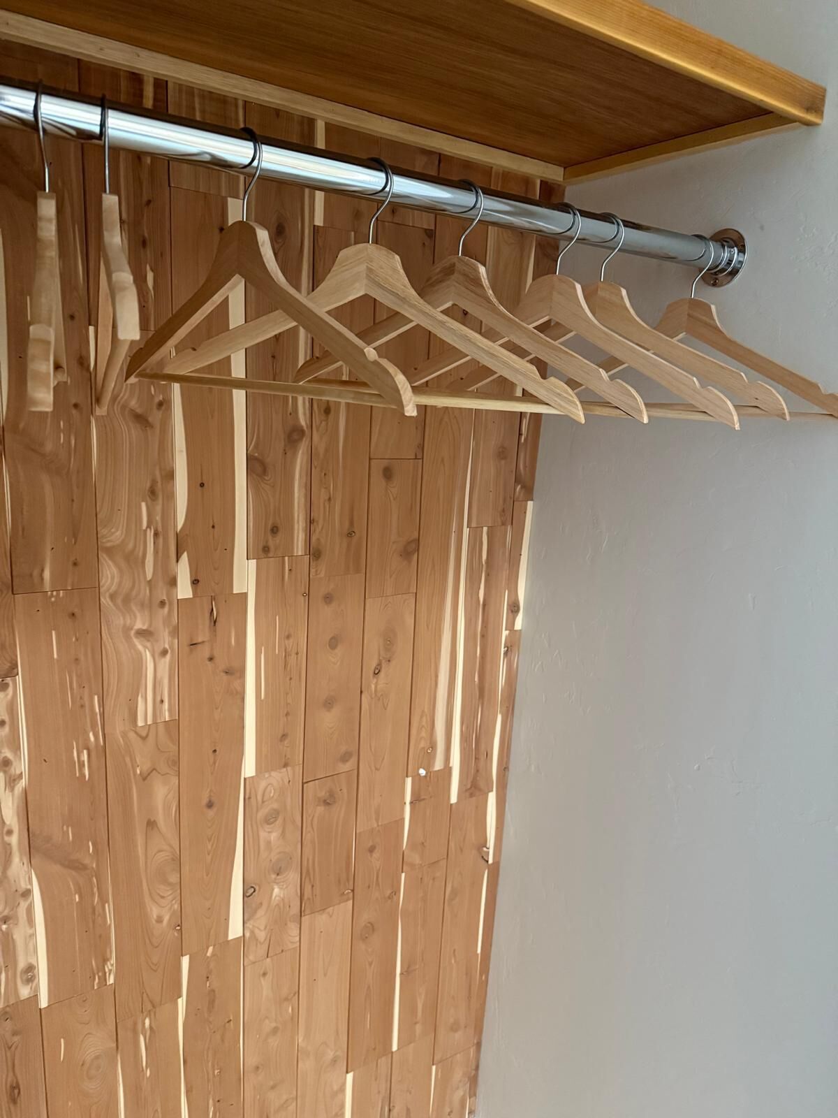 A wooden panel wall with a metal curtain rod and wooden hangers.