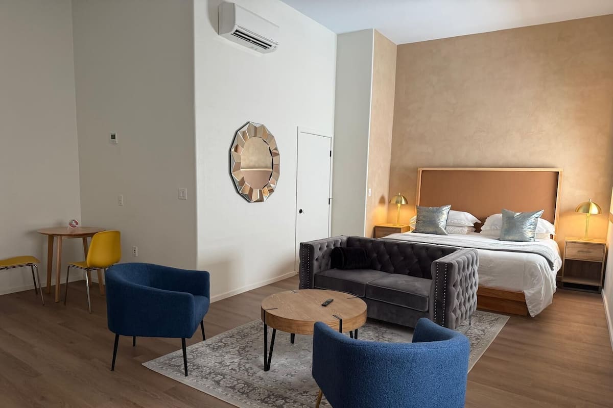 Moderni hotellihuone, jossa on suuri sänky, sohva, kaksi nojatuolia, pieni pöytä ja koristeellinen peili.
