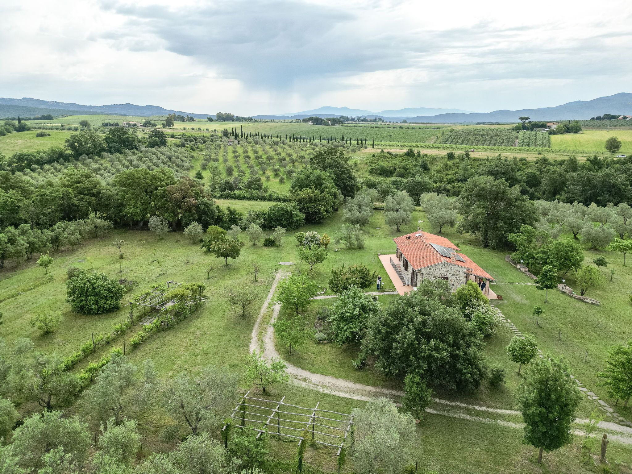 A rural landscape with a stone building featuring a red roof, surrounded by lush green fields and scattered trees.