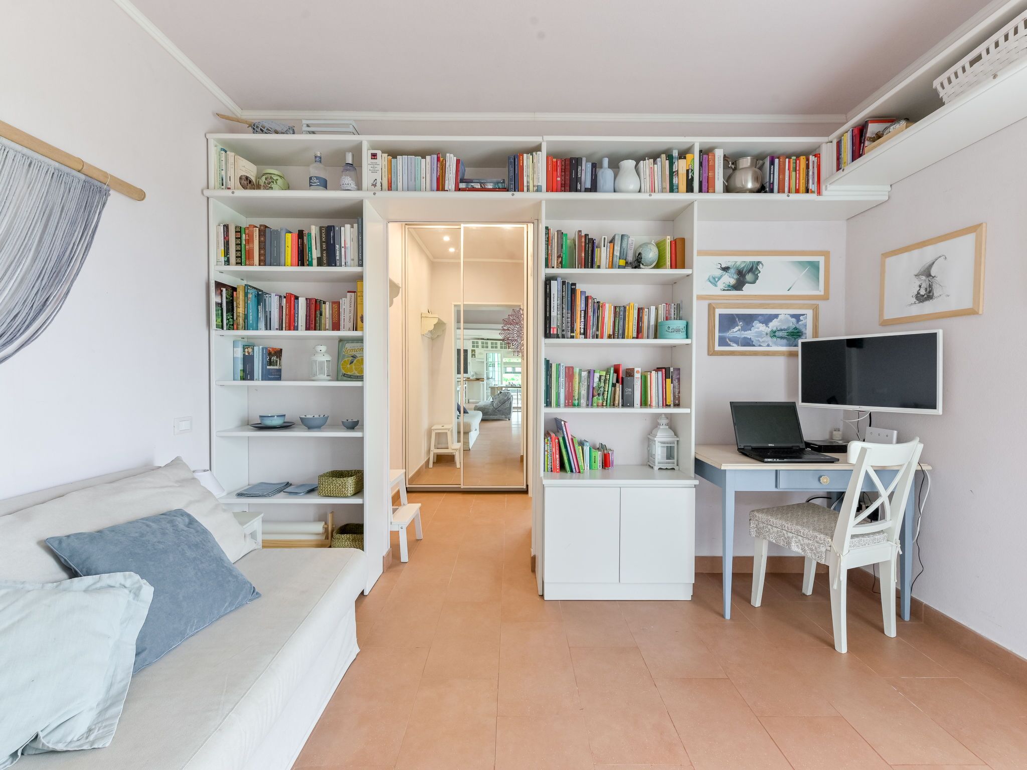 A compact living space with a sofa, a desk with a laptop, and a bookshelf filled with books.