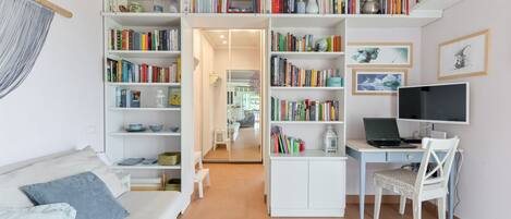 A compact living space with a sofa, a desk with a laptop, and a bookshelf filled with books.