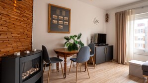 Un soggiorno moderno con una parete in legno, una composizione di foto incorniciate, un camino, un tavolo da pranzo con sedie, una TV e un'ampia finestra con tende.