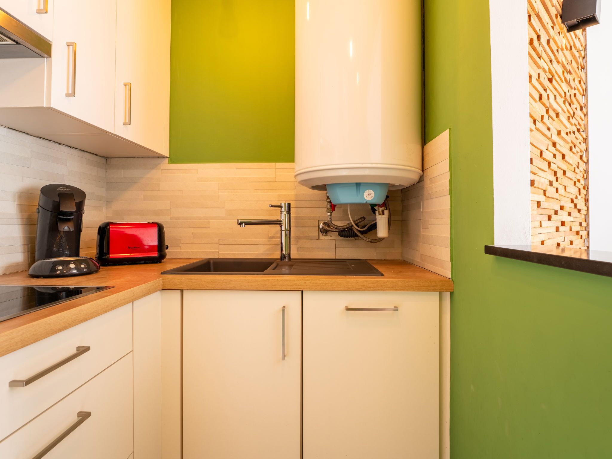 Una cocina compacta con cafetera integrada, tostadora y un lavamanos con grifo moderno.