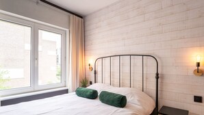 Una camera da letto con un letto, due cuscini verdi, un comodino, una lampada e una finestra con tende.