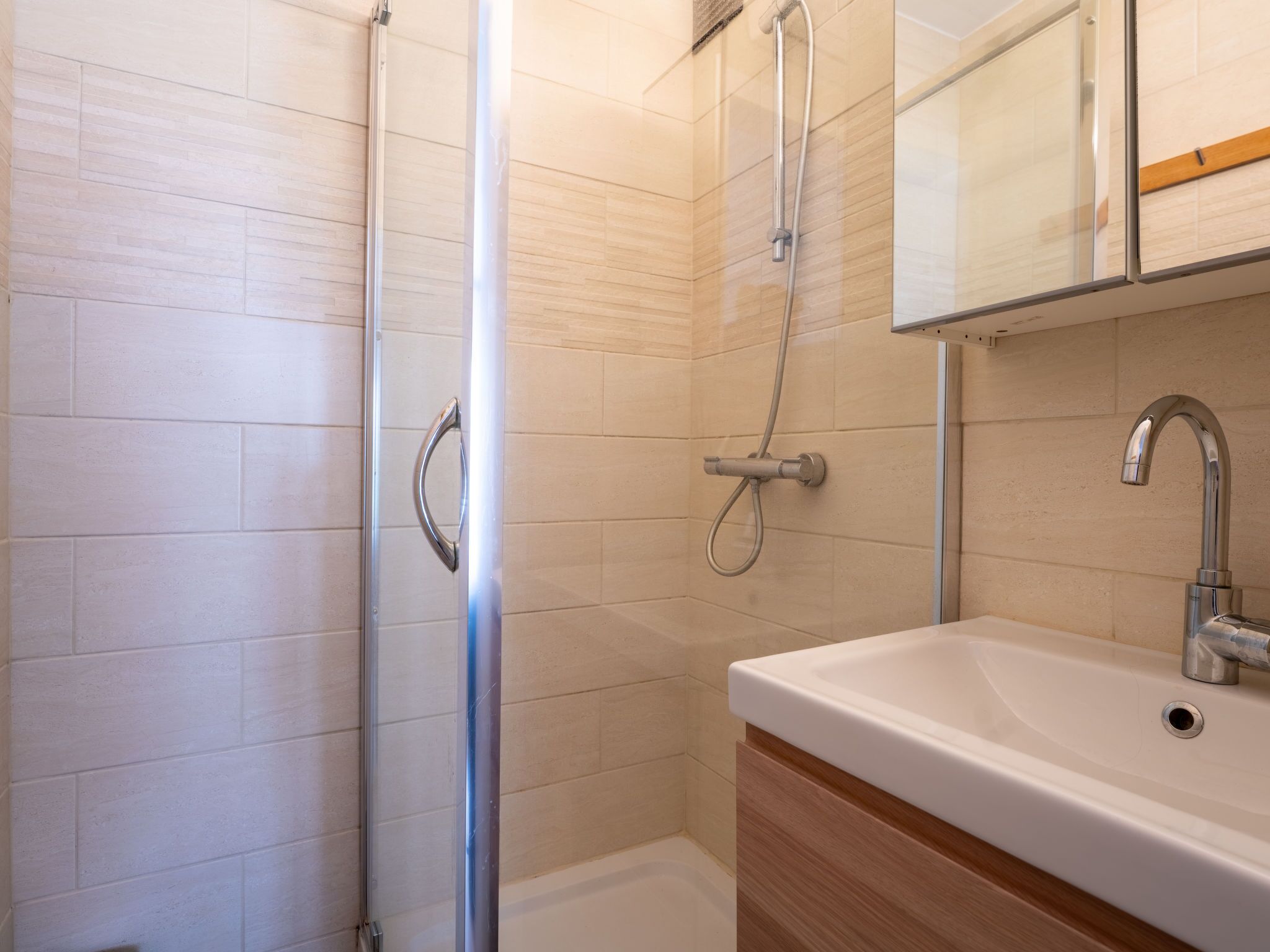 A modern bathroom with a glass shower enclosure, a white sink, and a wooden vanity.