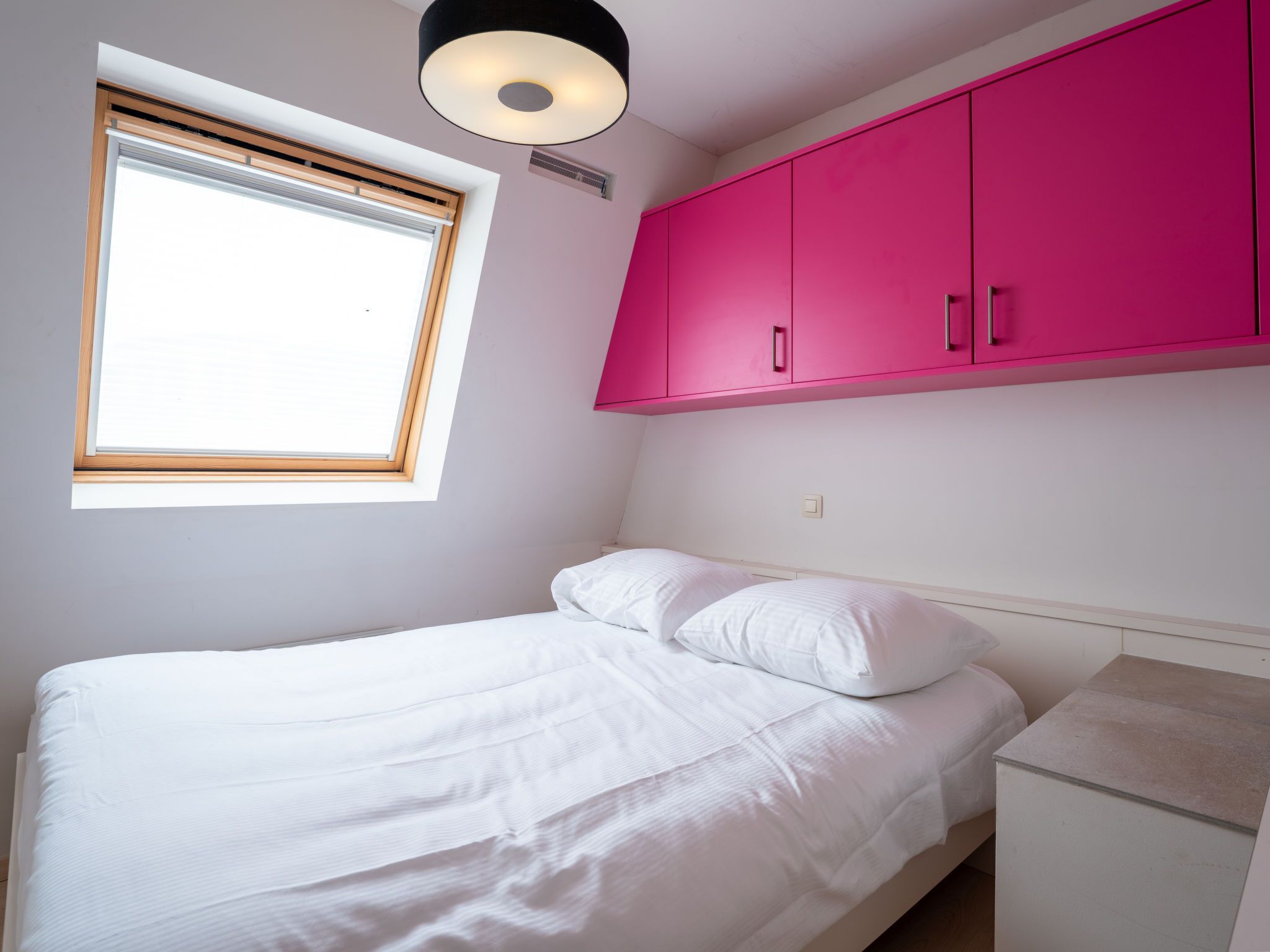 Ein Schlafzimmer mit einem Bett, einem Fenster mit Jalousien, einer Deckenleuchte und rosa Schränken.