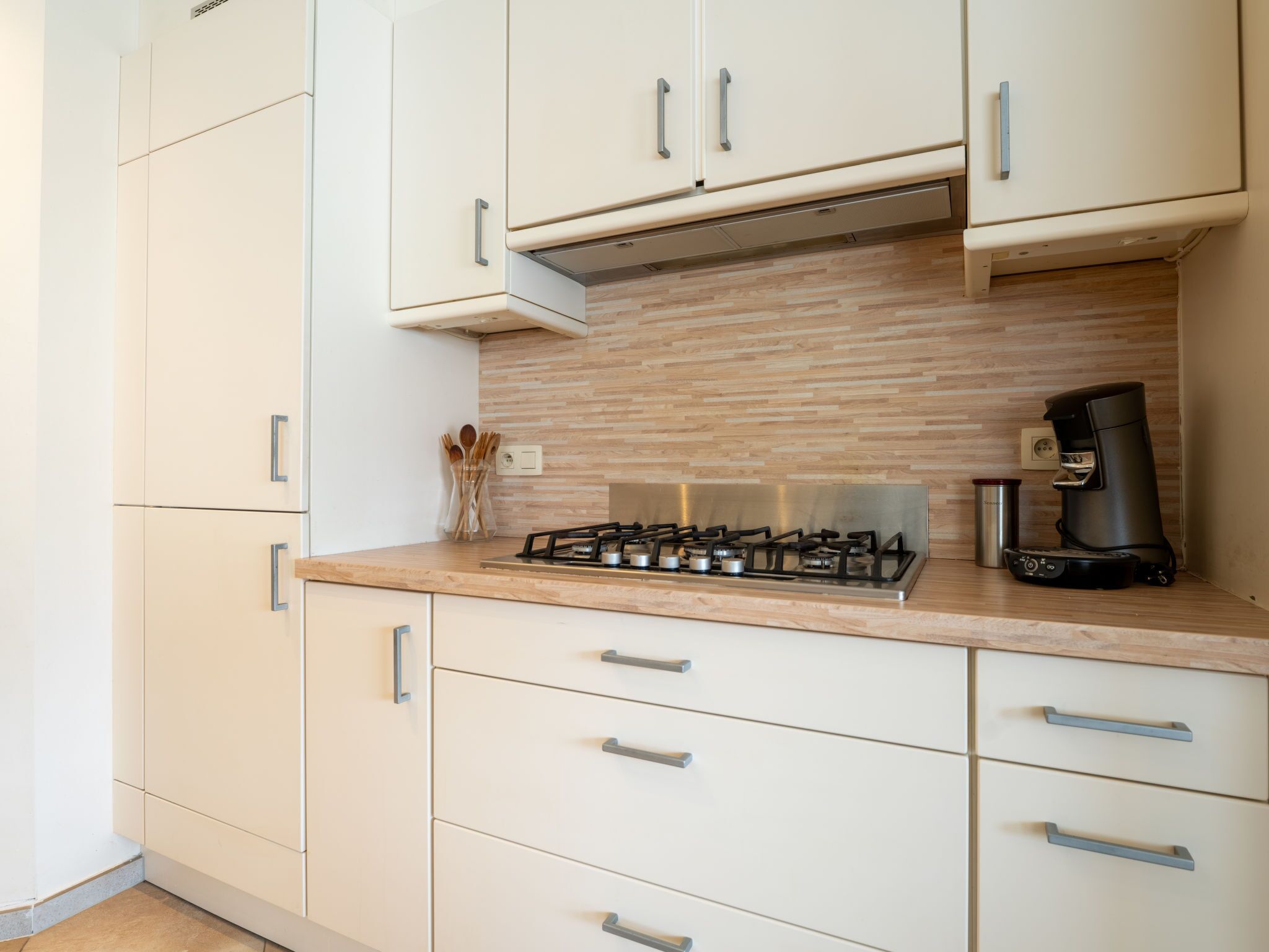 Una cocina moderna con armarios blancos, estufa a gas y cafetera.