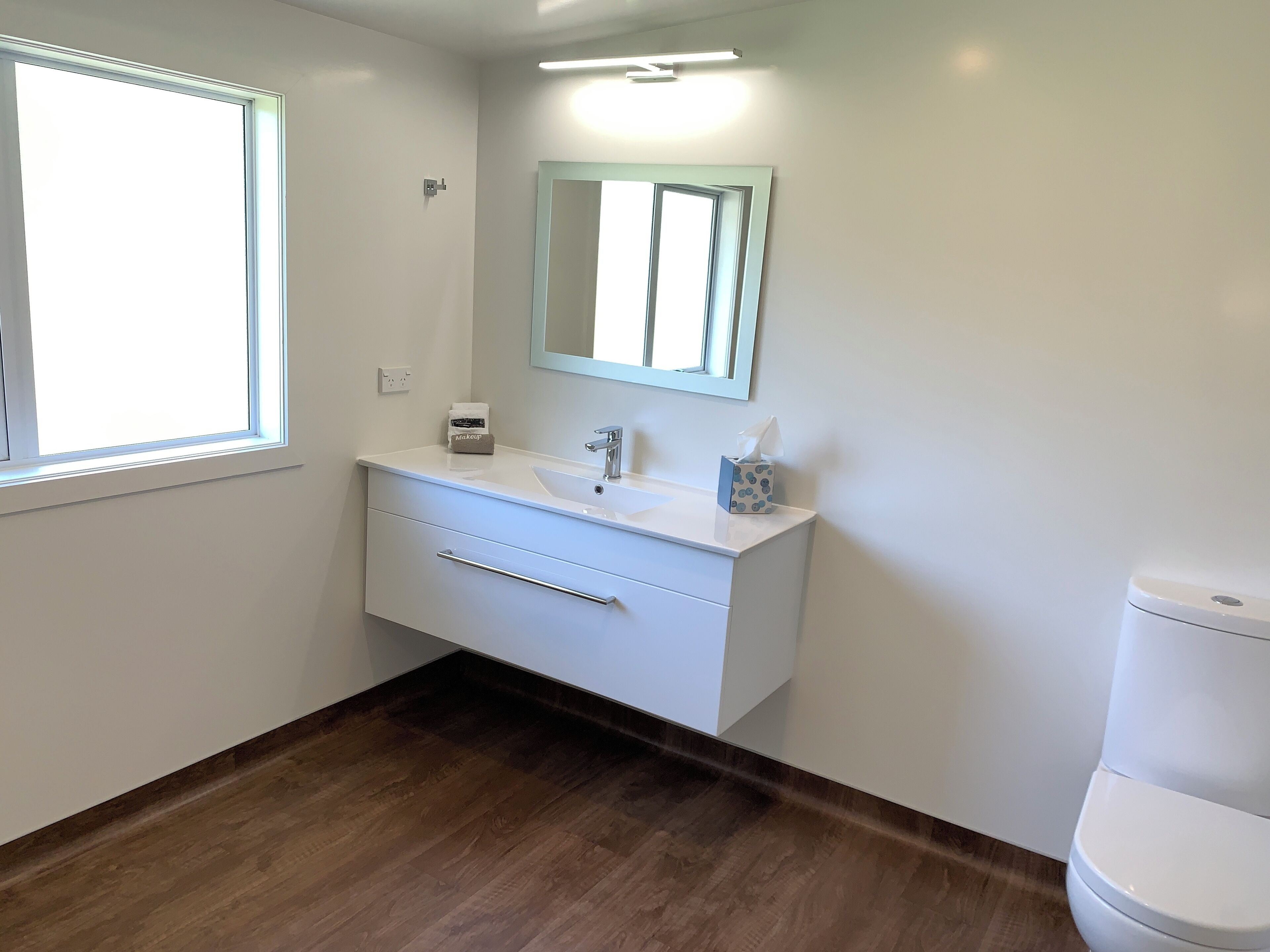 A bathroom with a white vanity, a mirror, a toilet, and a window.