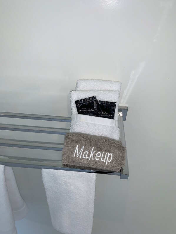 Une salle de bain avec un porte-serviettes sur lequel sont posés une serviette blanche, une serviette grise et une trousse de maquillage noire.