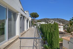 A modern building with a balcony, a neatly trimmed hedge, and a view of a hillside with buildings. - Villa Puerto de Soller el Portet (Moraira)