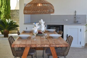 A wooden dining table set with white bowls, wine glasses, and a wicker overhead light fixture. - Villa Puerto de Soller el Portet (Moraira)