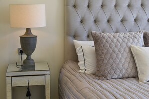 A neatly made bed with a tufted headboard, a bedside table with a lamp, and a drawer.