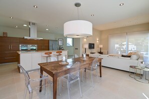 A modern kitchen with a dining area, featuring a wooden table, clear chairs, and a large pendant light. - Villa Puerto de Soller el Portet (Moraira)