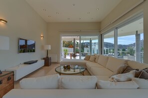 Una sala de estar moderna con un sofá grande, una mesa de centro de vidrio y un televisor de pantalla plana montado en la pared.