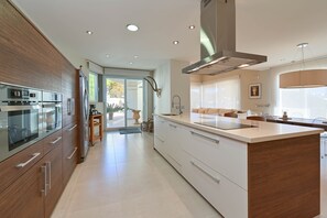 Una cocina moderna con una isla grande, electrodomésticos de acero inoxidable y un ventanal corredero que da a un patio.