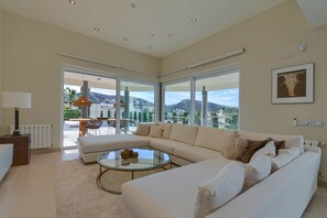 Un salon spacieux avec un grand canapé d’angle, une table basse en verre et une vue sur un balcon aménagé avec du mobilier d’extérieur.