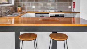 A modern kitchen with a wooden countertop, stainless steel appliances, and two bar stools. - Retreat on Reid Street (Merimbula)