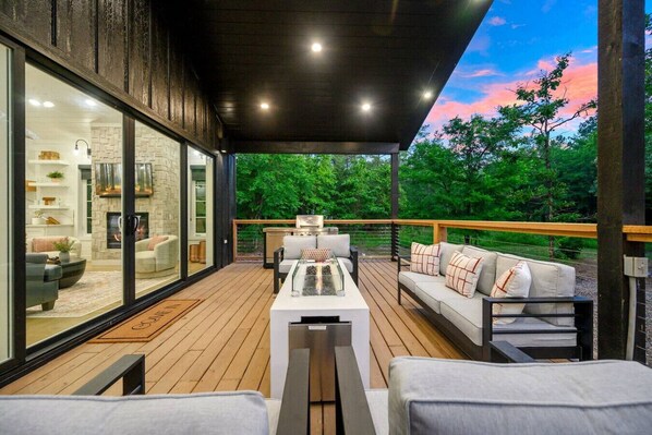 Une terrasse extérieure moderne avec un mur de verre, une cheminée et un canapé.
