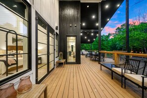 A wooden deck with outdoor seating, a view of a bedroom with a bed and window, and a dark wall with a door.