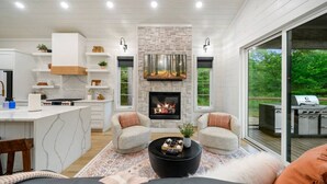 Una cocina moderna con armarios blancos, una isla central y una chimenea. Hay dos zonas de estar con sofás y una mesa de centro.