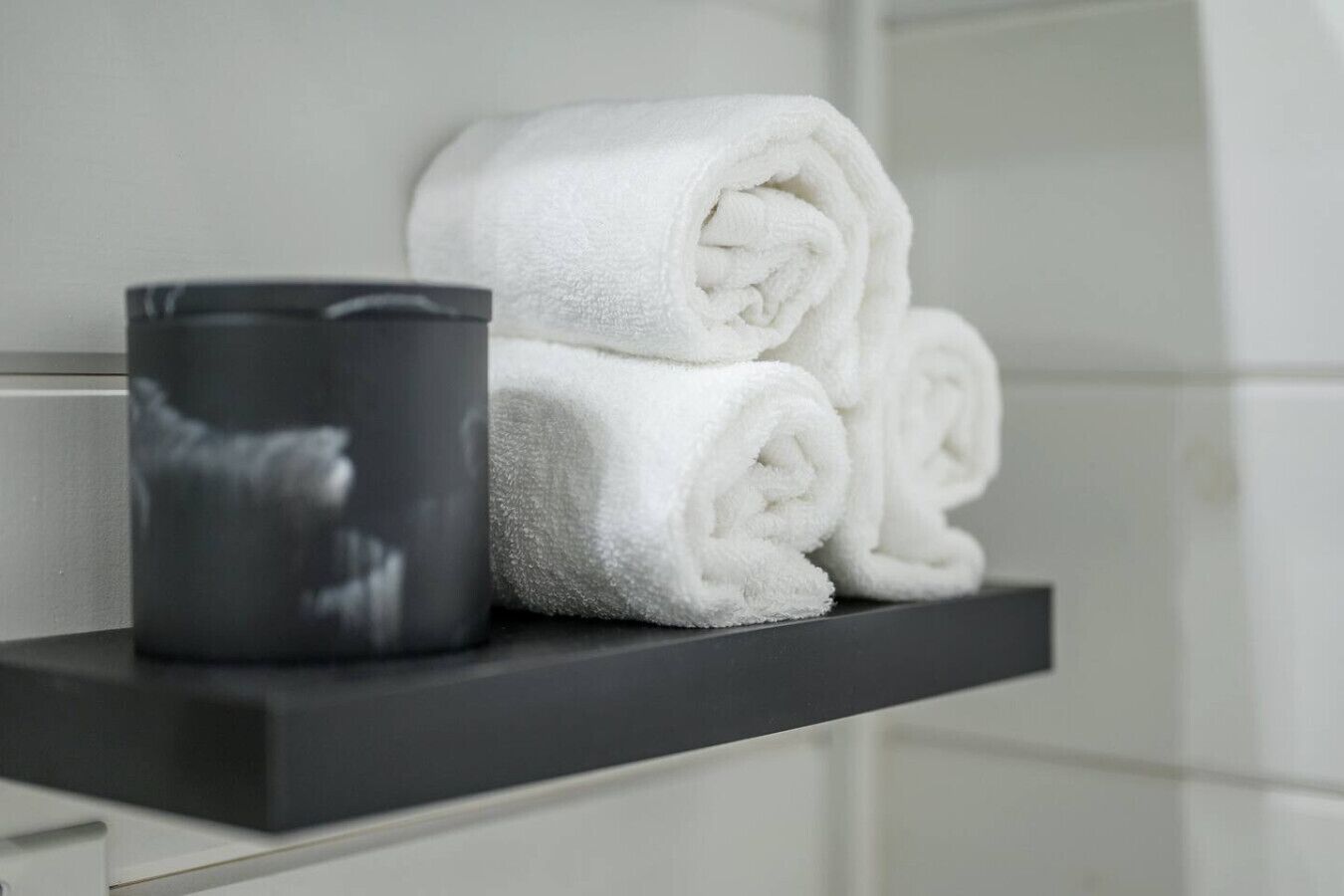 A bathroom with a towel rack holding rolled towels and a black container.