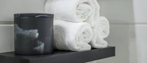 A bathroom with a towel rack holding rolled towels and a black container.