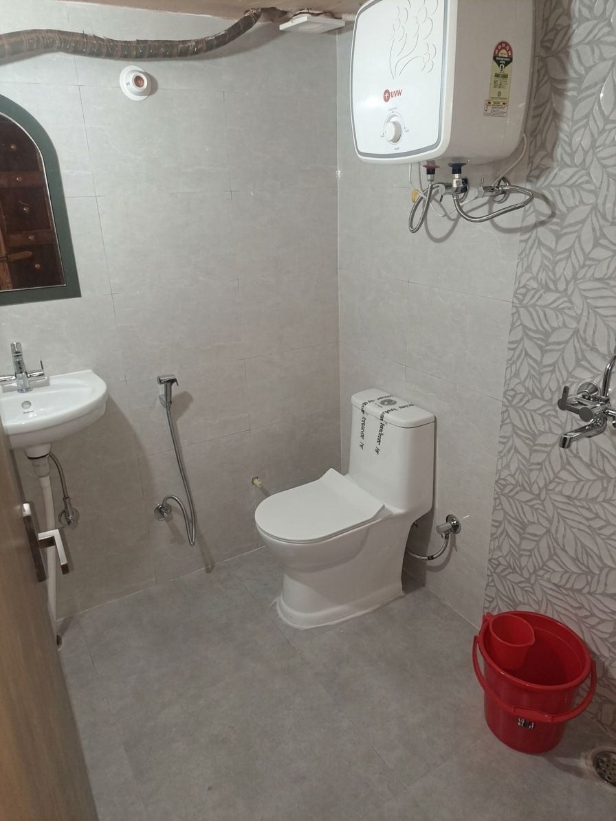 Een badkamer met toilet, wastafel, douche en een rode emmer.