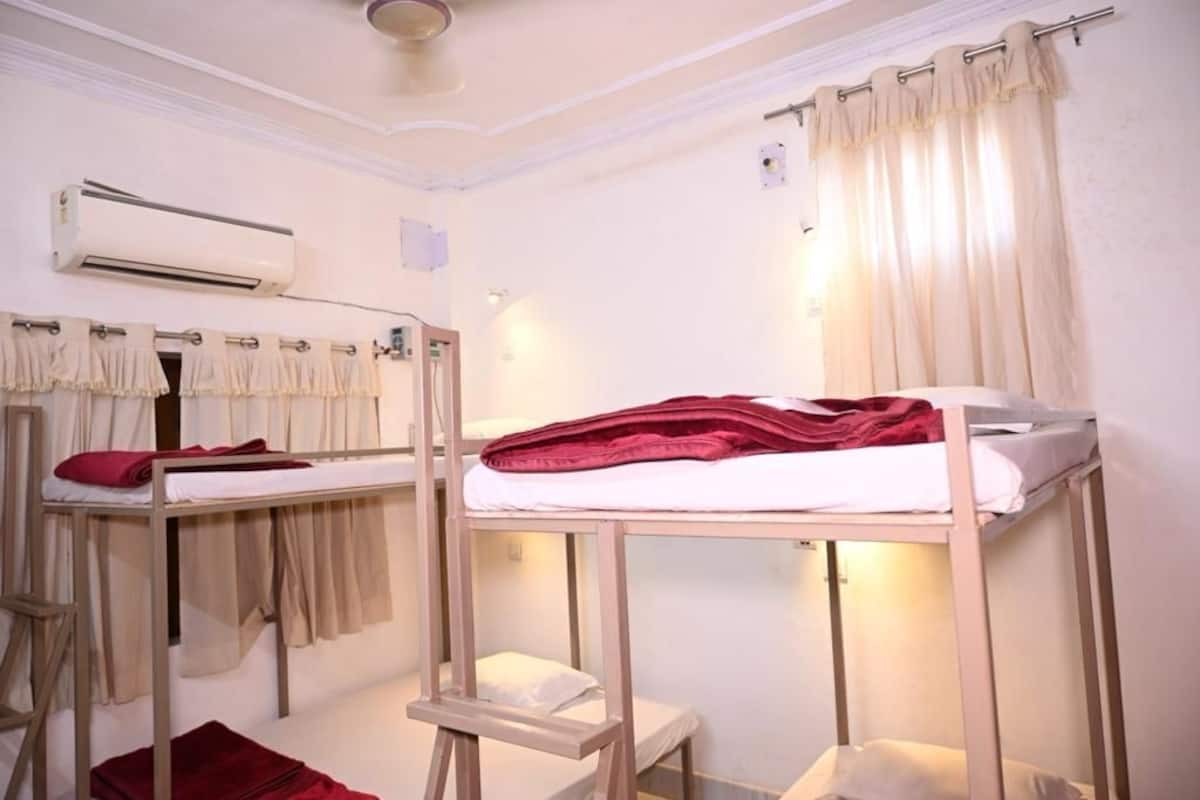A dormitory room with bunk beds, a mirror, an air conditioning unit, and a curtain.
