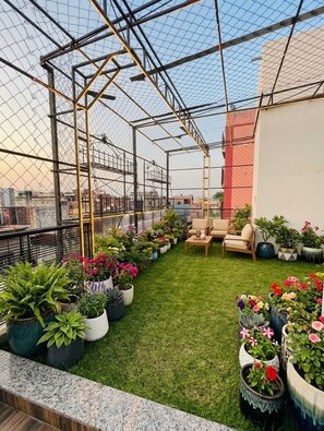 A rooftop garden with a metal fence, potted plants, and outdoor furniture. - Batra Guest House (Varanasi)