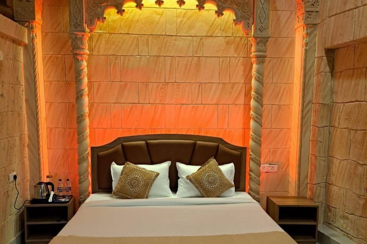 A large bed with a wooden headboard, two bedside tables, and a decorative wall with a patterned ceiling light.