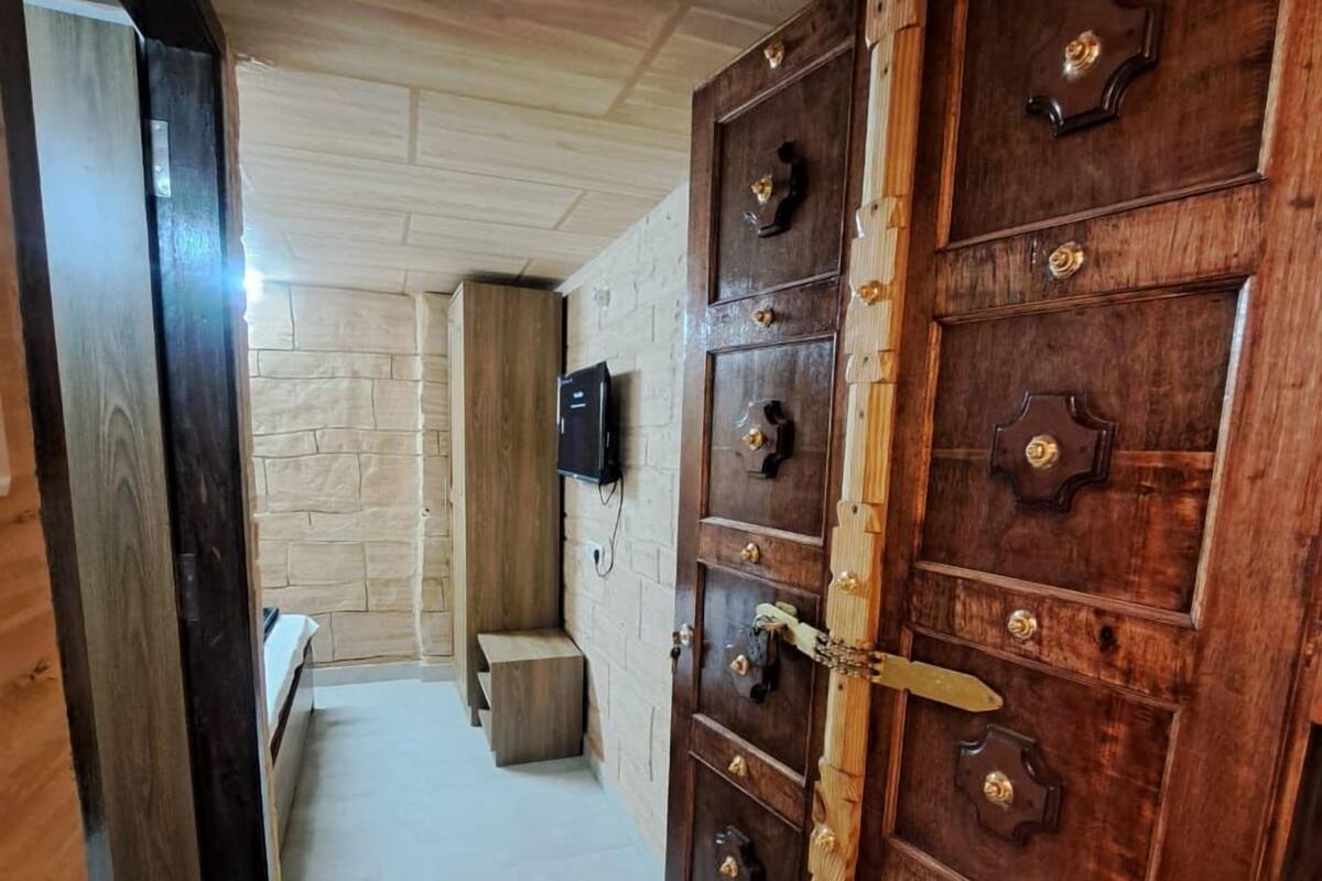 A hallway with a large wooden door with multiple locks and a television mounted on the wall.
